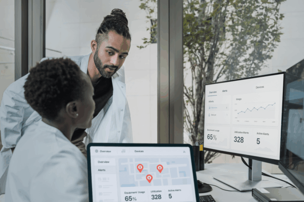 Two healthcare professionals using an automated tracking dashboard on a computer to streamline hospital operations and improve data accuracy for medical assets.